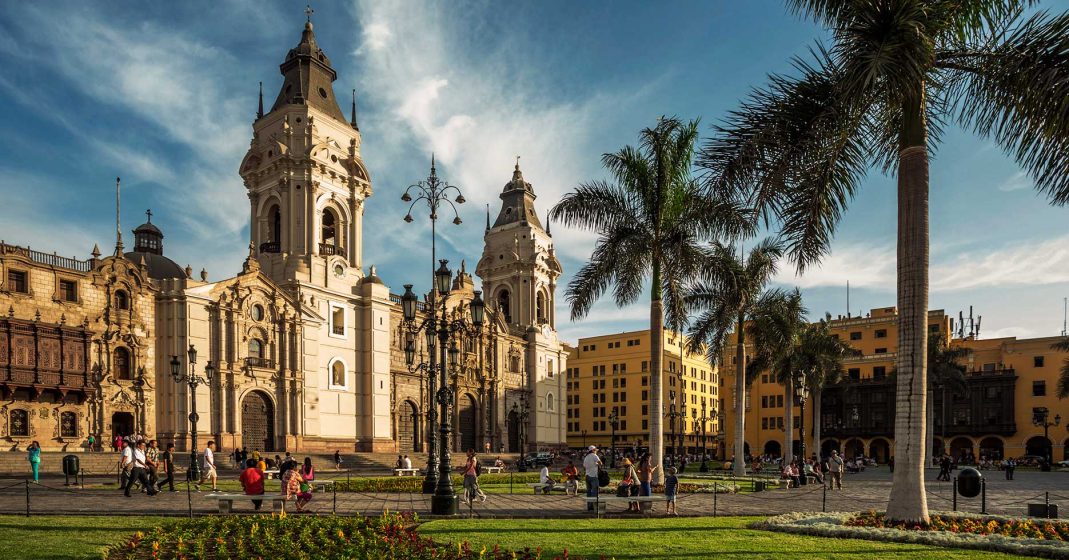 Luxury trip to Peru through Lima, view of the Plaza de Armas with people, the cathedral, and palm trees.