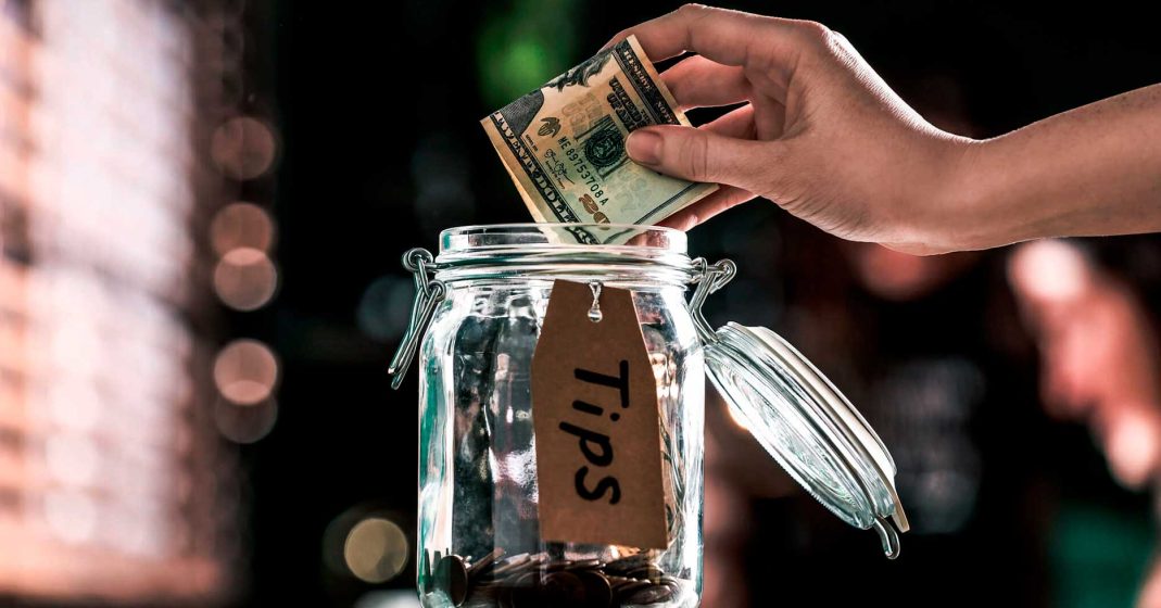 Hand giving a $20 tip in a glass container